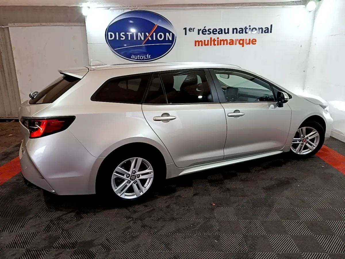 Vue de profil droit d'une Suzuki Swace 1.8 Hybrid Privilège gris clair en stationnement intérieur sur sol à motifs.