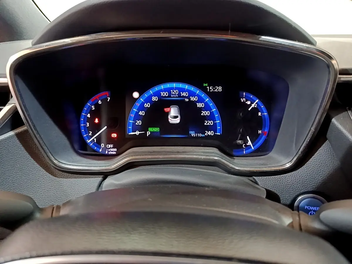 Vue rapprochée du tableau de bord numérique bleu de la Suzuki Swace 1.8 Hybrid Privilege avec volant partiellement visible.