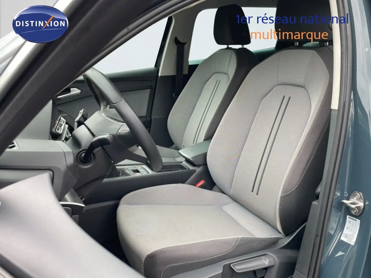 Vue intérieure côté conducteur du SEAT LEON ST 2025 bleu Fjord, mettant en valeur les sièges tissu gris clair et tableau de bord.