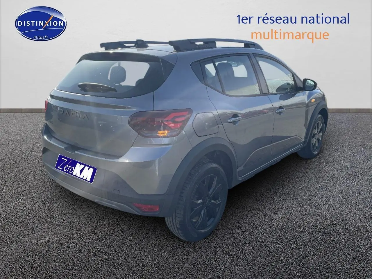 Vue 3/4 arrière droit d'une Dacia Sandero gris schiste avec barres de toit et jantes alu noires.