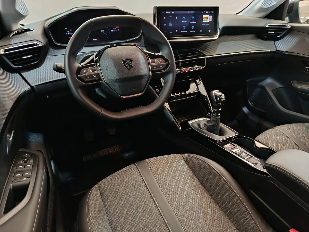 Intérieur de la Peugeot 208 gris clair, vue côté conducteur sur le volant cuir et écran tactile central.