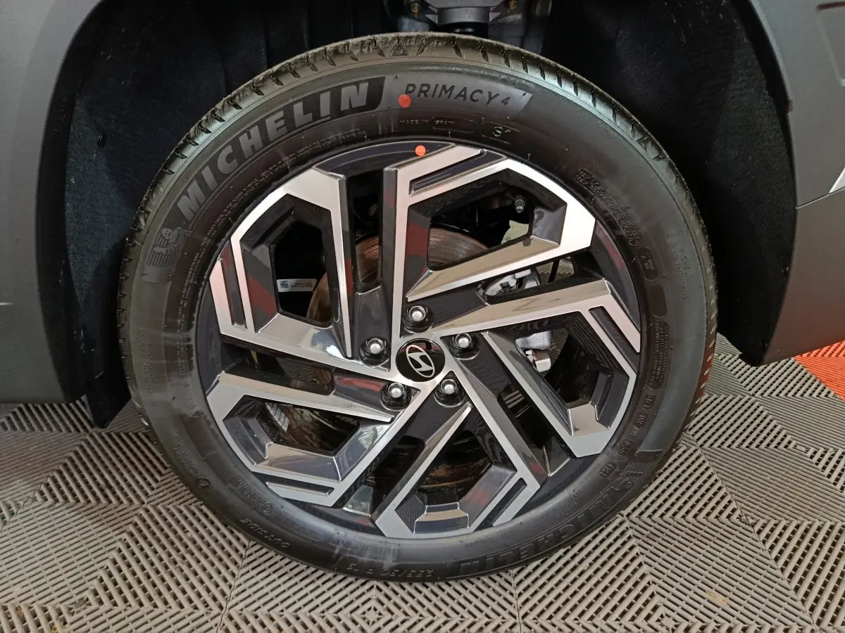 Gros plan sur la roue avant droite du Hyundai Tucson gris clair 2025, jante alliage au design géométrique moderne.