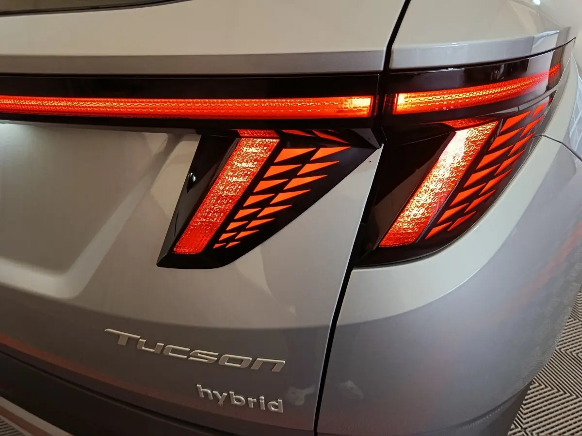 Gros plan sur le feu arrière droit rouge allumé du Hyundai Tucson gris clair avec logo Tucson et hybrid visible.