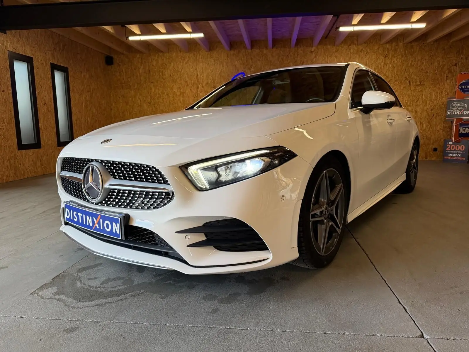 Vue 3/4 avant droite d'une Mercedes Classe A 220D AMG Line blanche avec calandre diamant et jantes AMG foncées.