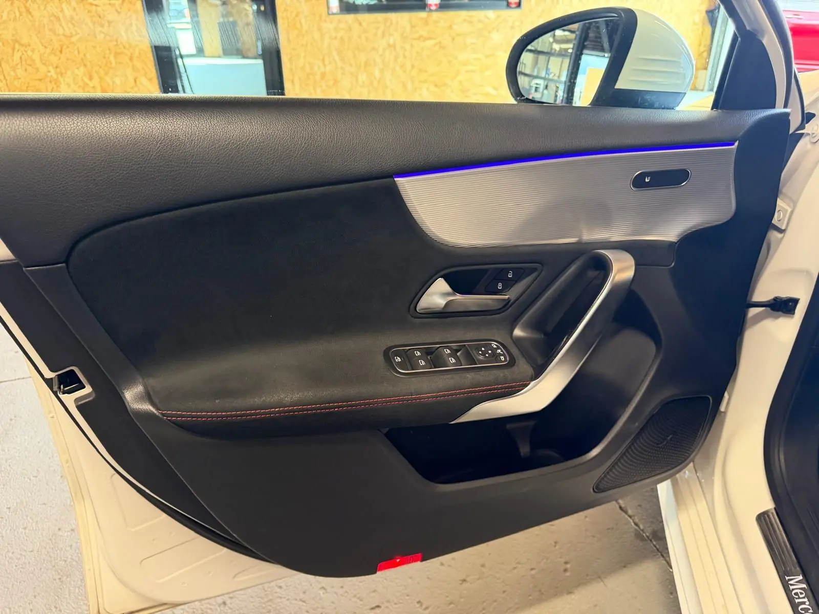 Vue intérieure côté gauche de la porte avant blanche d'une Mercedes Classe A 220D AMG Line avec éclairage d'ambiance bleu.