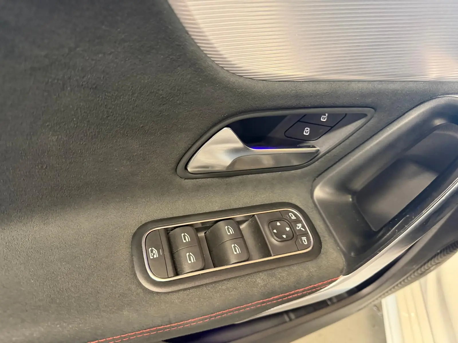 Détail de la porte côté gauche d’une Mercedes Classe A 220D AMG Line blanche, avec commandes de vitres et poignée intérieure.