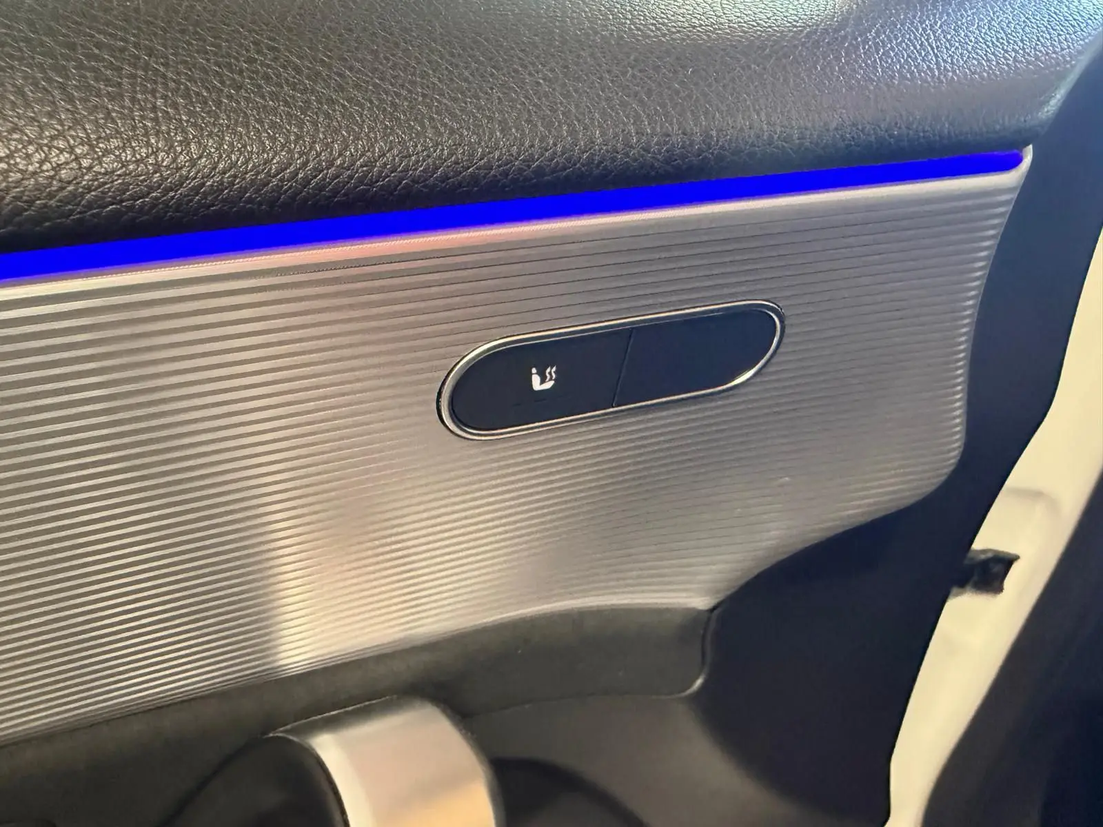 Détail de la porte intérieure côté gauche d’une Mercedes Classe A 220D AMG Line blanche, avec éclairage d’ambiance bleu et bouton de siège chauffant.