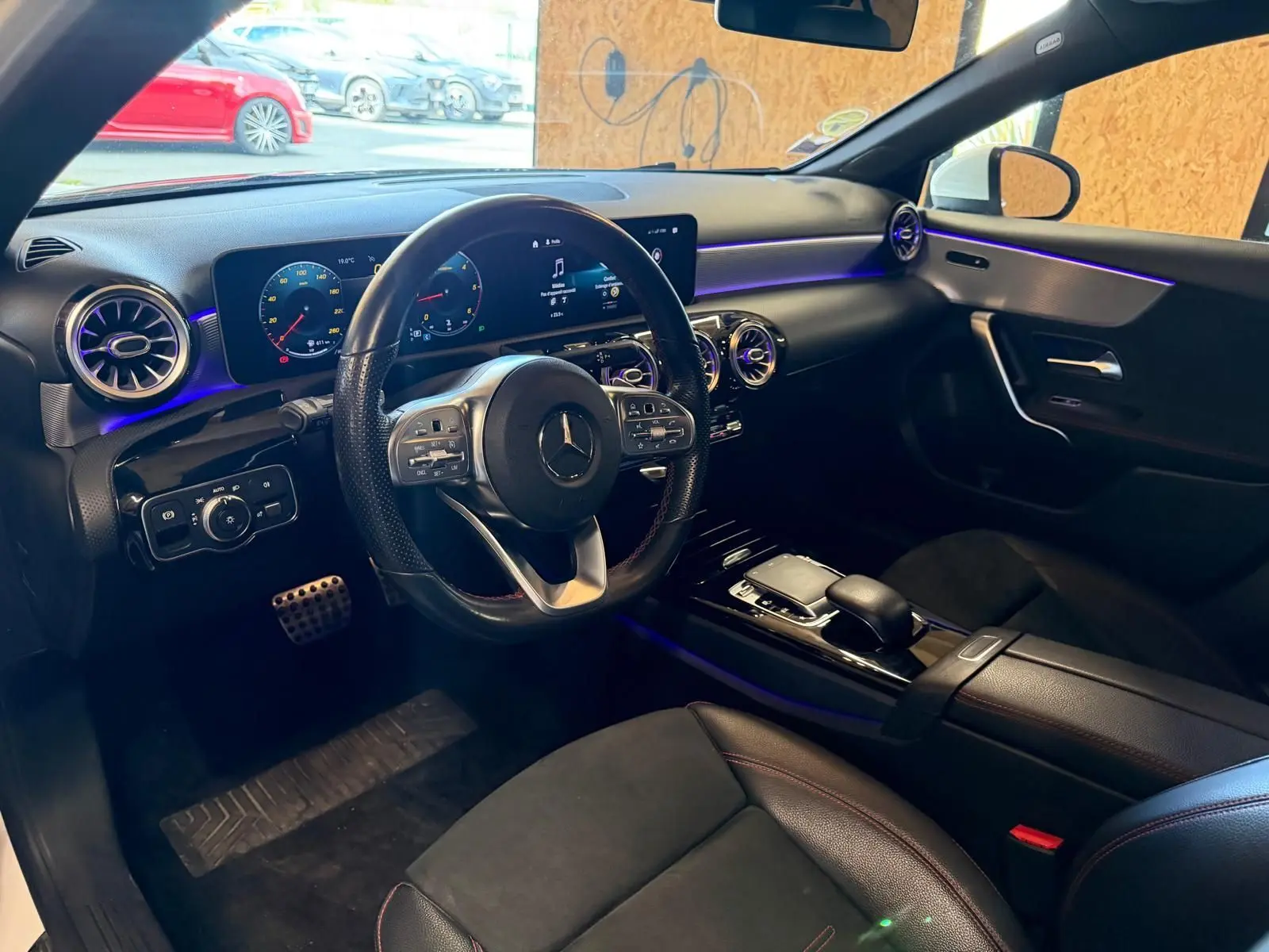 Vue intérieure côté conducteur de la Mercedes Classe A 220D AMG Line 2019 avec tableau de bord numérique et éclairage d'ambiance violet.
