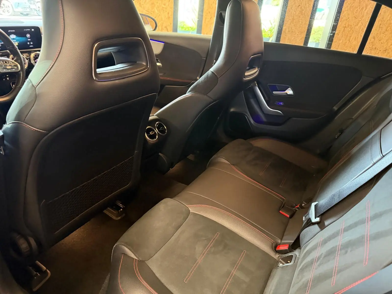 Vue intérieure arrière droite de la Mercedes Classe A 220D AMG Line 2019 avec sièges noirs et surpiqûres rouges.