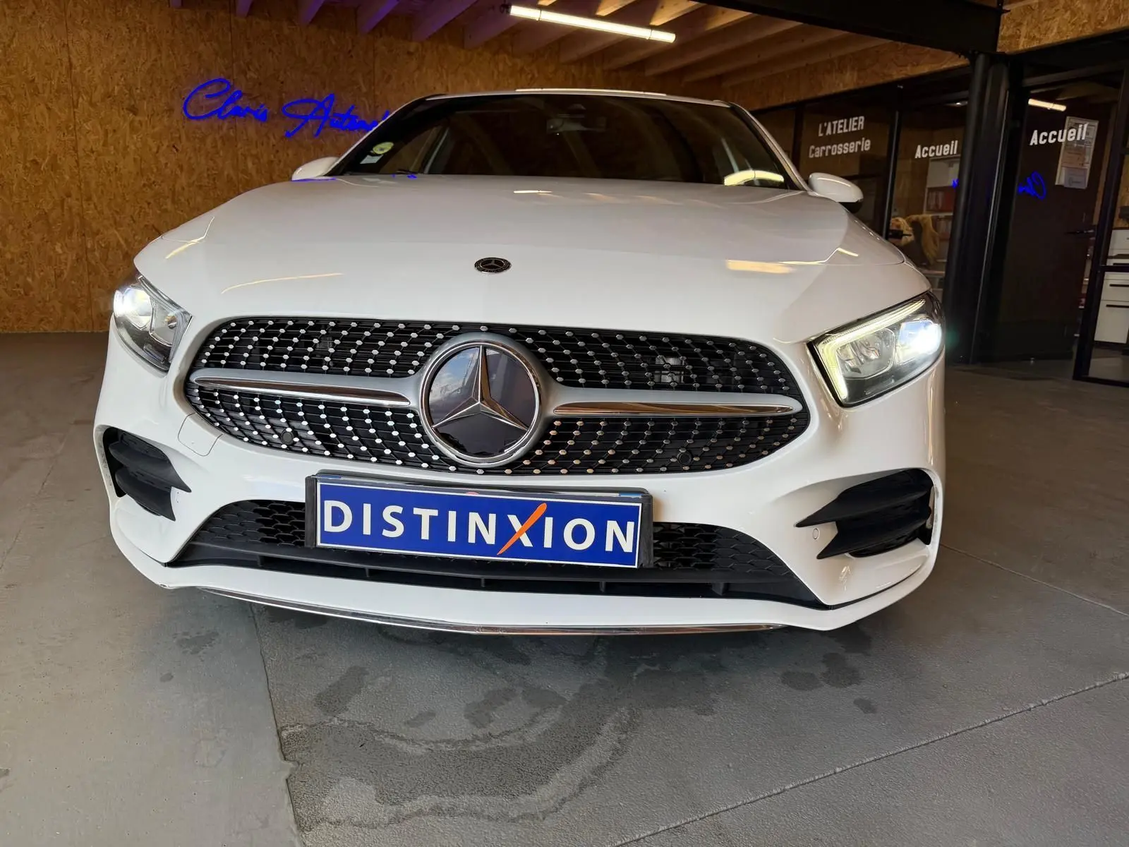 Vue avant d'une Mercedes Classe A 220D AMG Line blanche avec calandre diamantée et phares allumés en intérieur showroom.