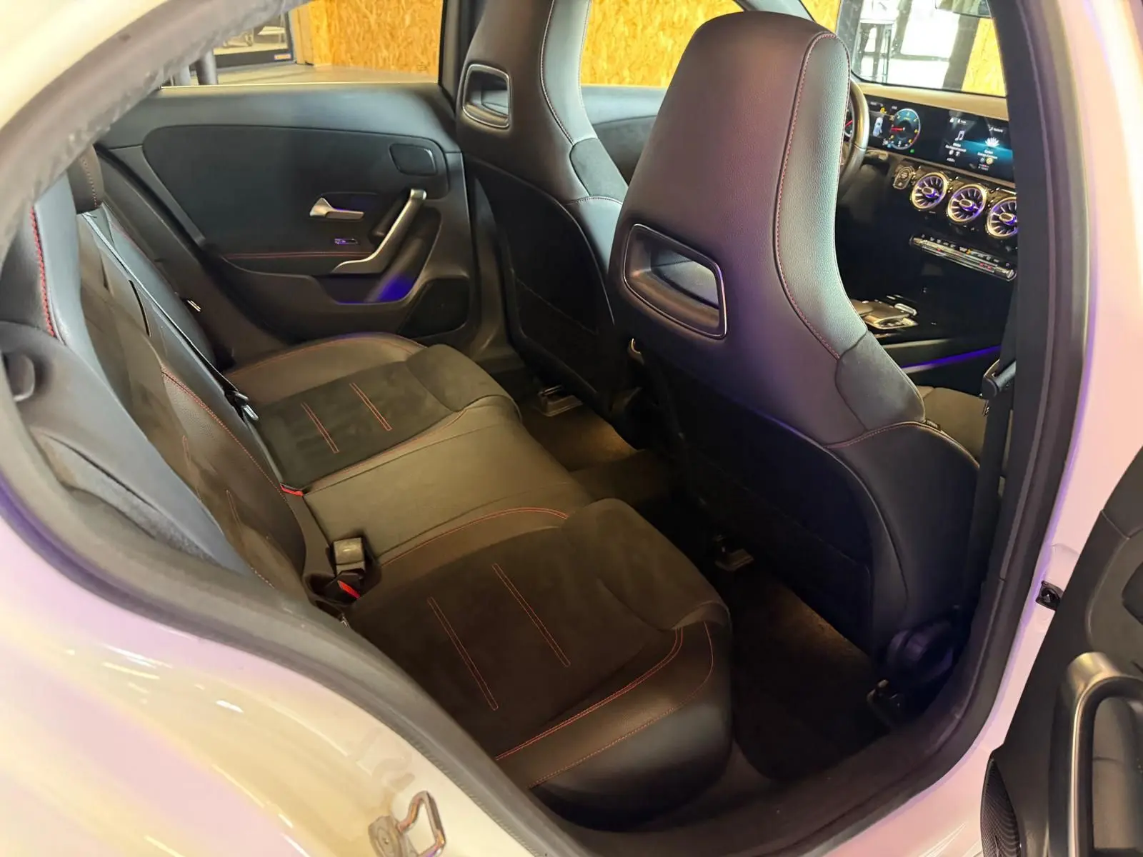 Vue intérieure depuis la porte arrière droite d'une Mercedes Classe A 220D AMG Line blanche, sièges noirs avec surpiqûres rouges.