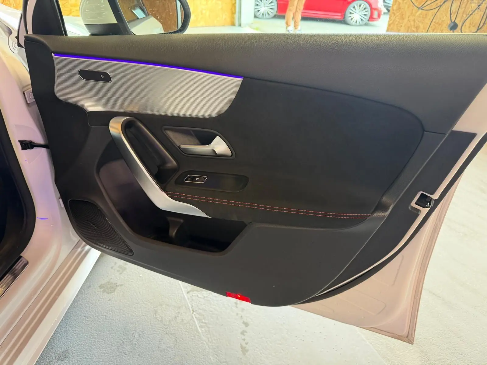 Vue intérieure côté gauche de la porte avant blanche d'une Mercedes Classe A 220D AMG Line avec éclairage d'ambiance violet.
