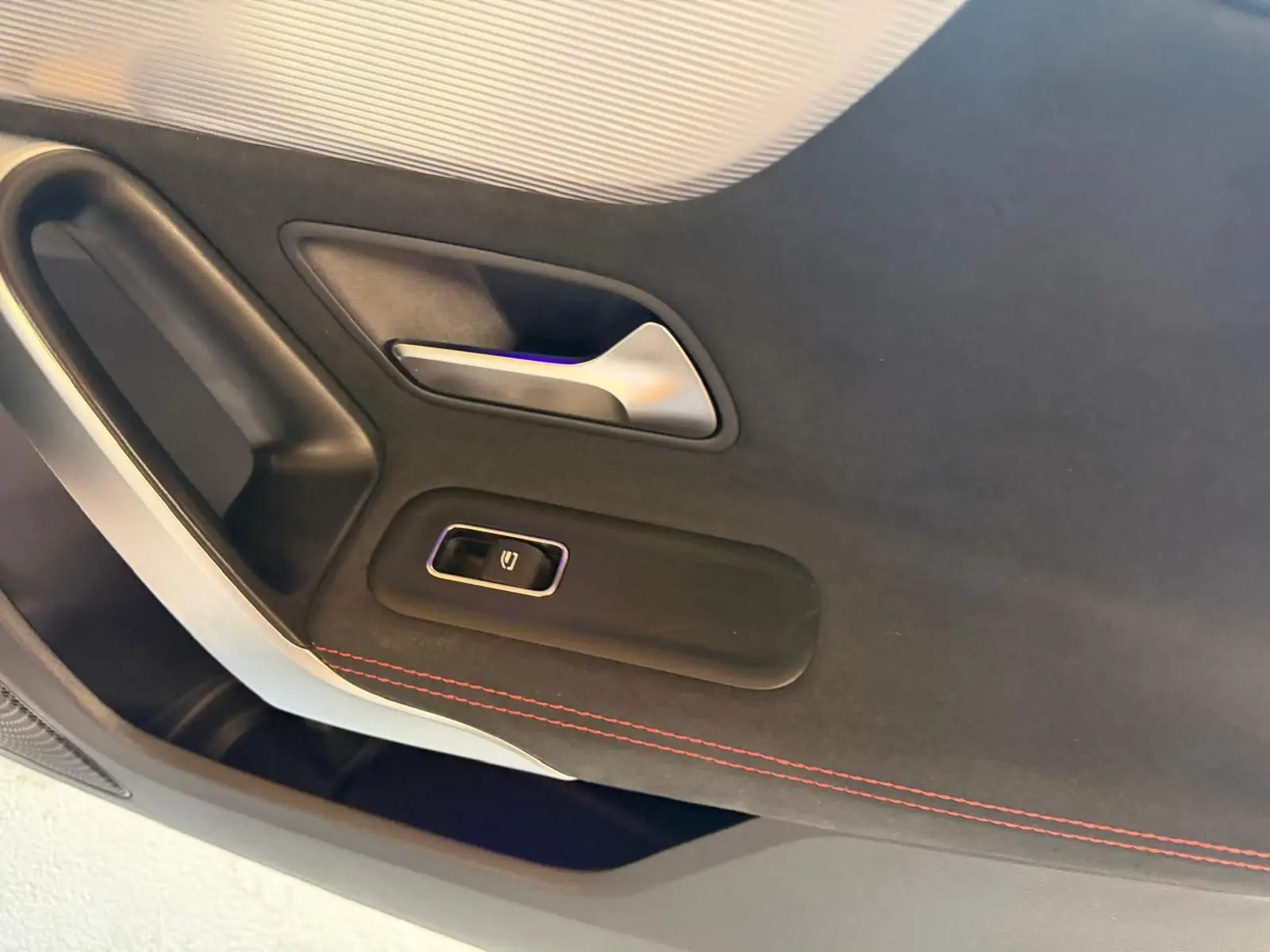 Détail de la porte intérieure côté gauche de la Mercedes Classe A 220D AMG Line blanche avec couture rouge et bouton de lève-vitre.