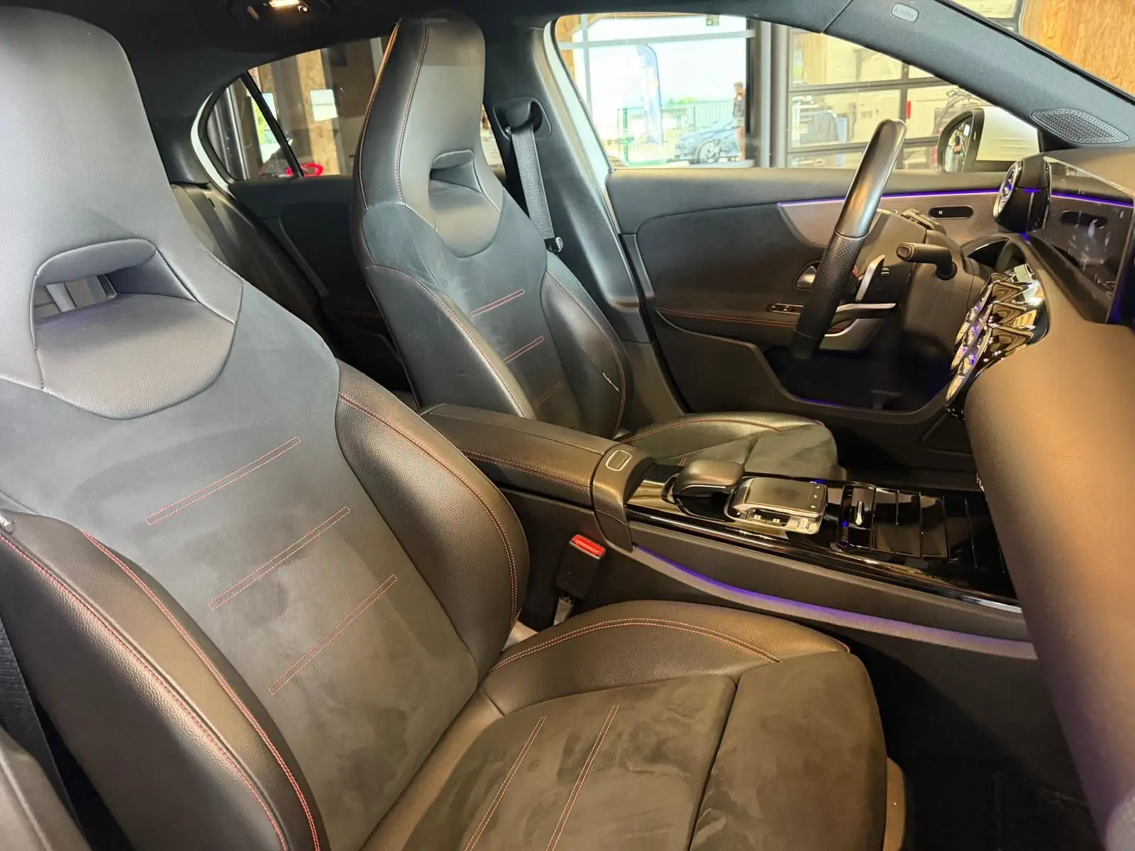 Vue intérieure côté conducteur de la Mercedes Classe A 220D AMG Line 2019 avec sièges sport noirs et surpiqûres rouges.