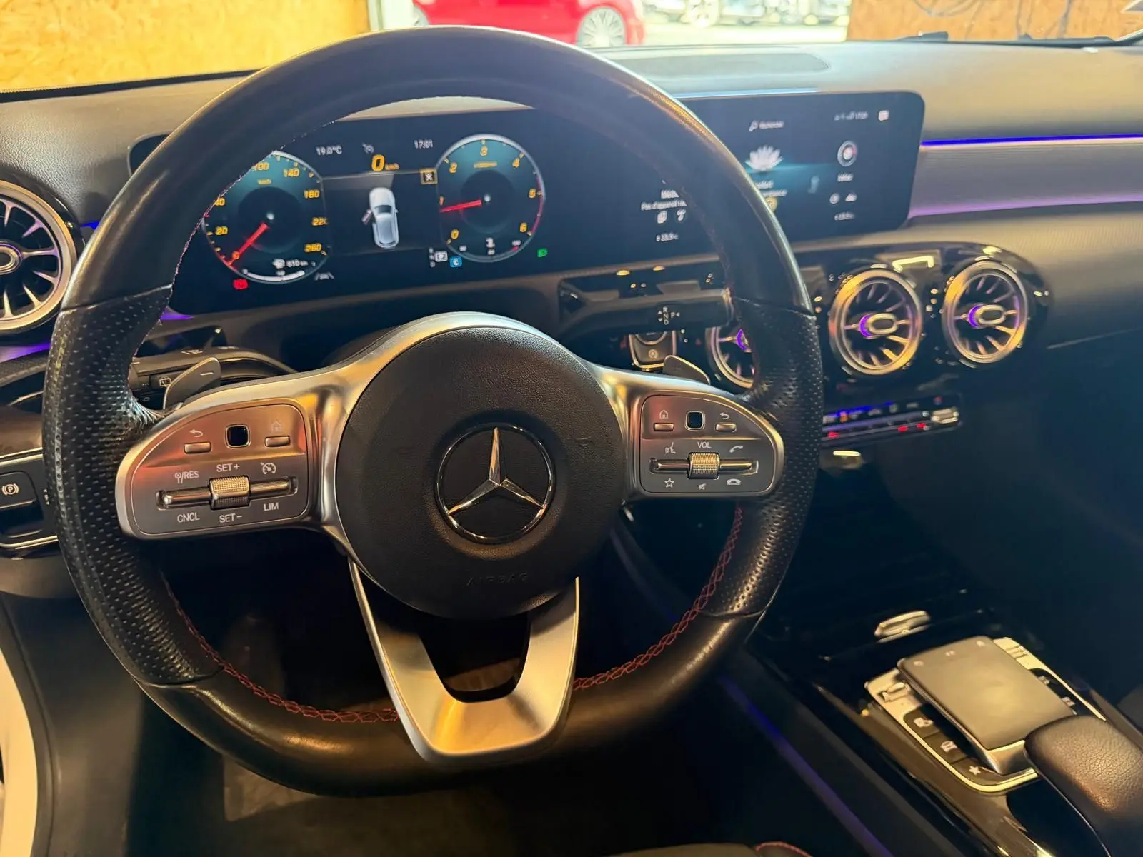 Vue intérieure centrée sur le volant cuir noir de la Mercedes Classe A 220D AMG Line avec tableau de bord numérique et éclairage d'ambiance.