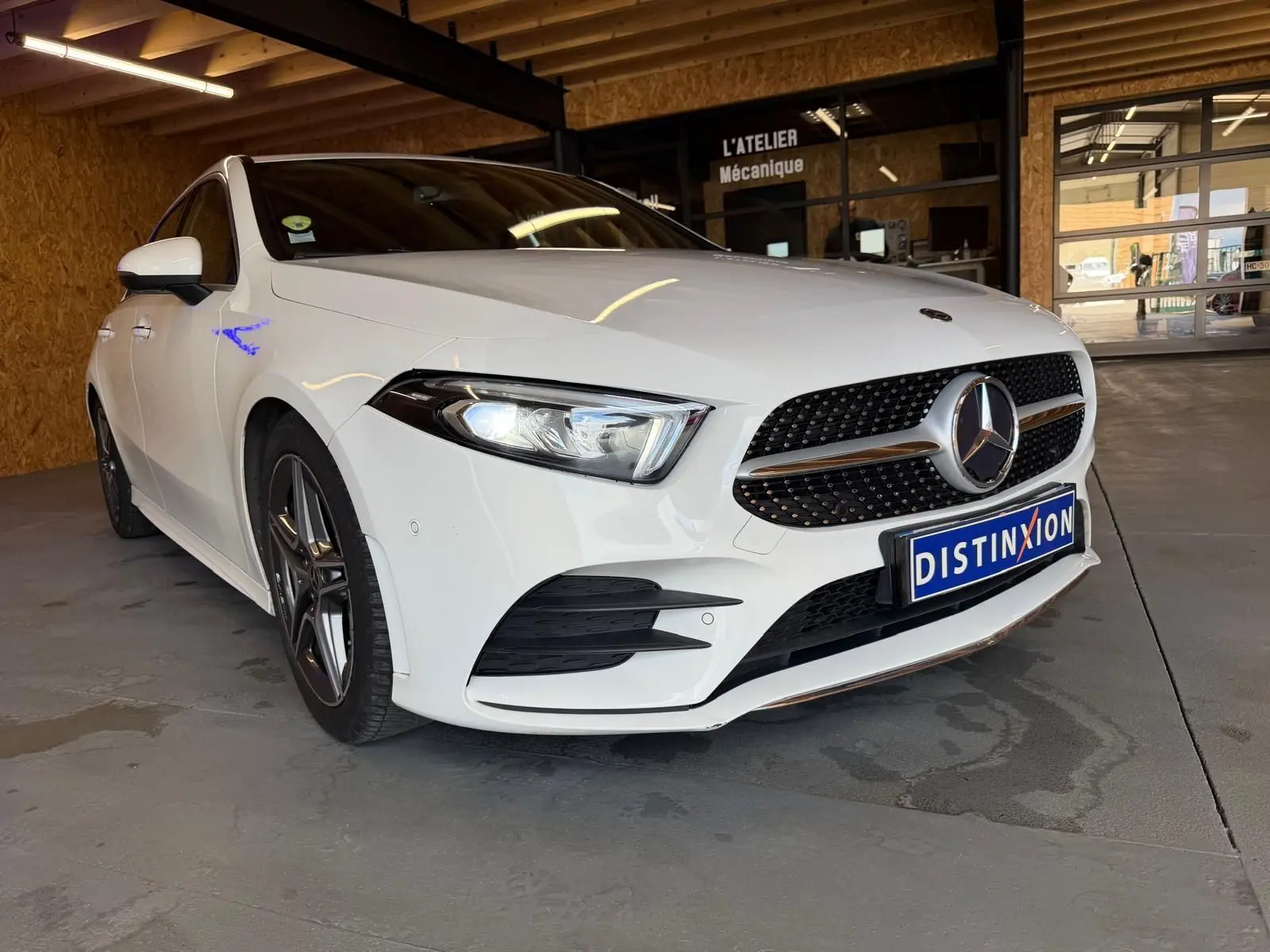 Mercedes Classe A 220D AMG Line blanche vue en 3/4 avant droit dans un garage avec calandre sportive et phares allumés.