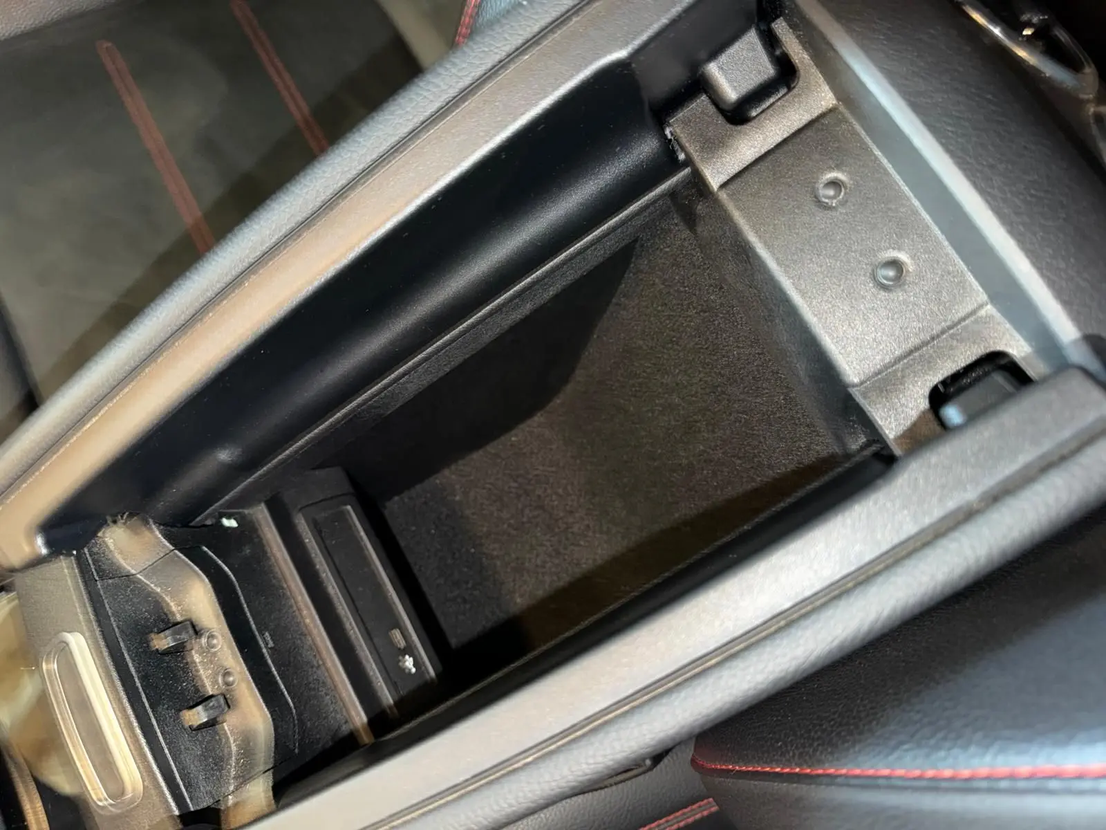 Vue rapprochée de la console centrale ouverte d’une Mercedes Classe A 220D AMG Line avec intérieur noir et surpiqûres rouges.