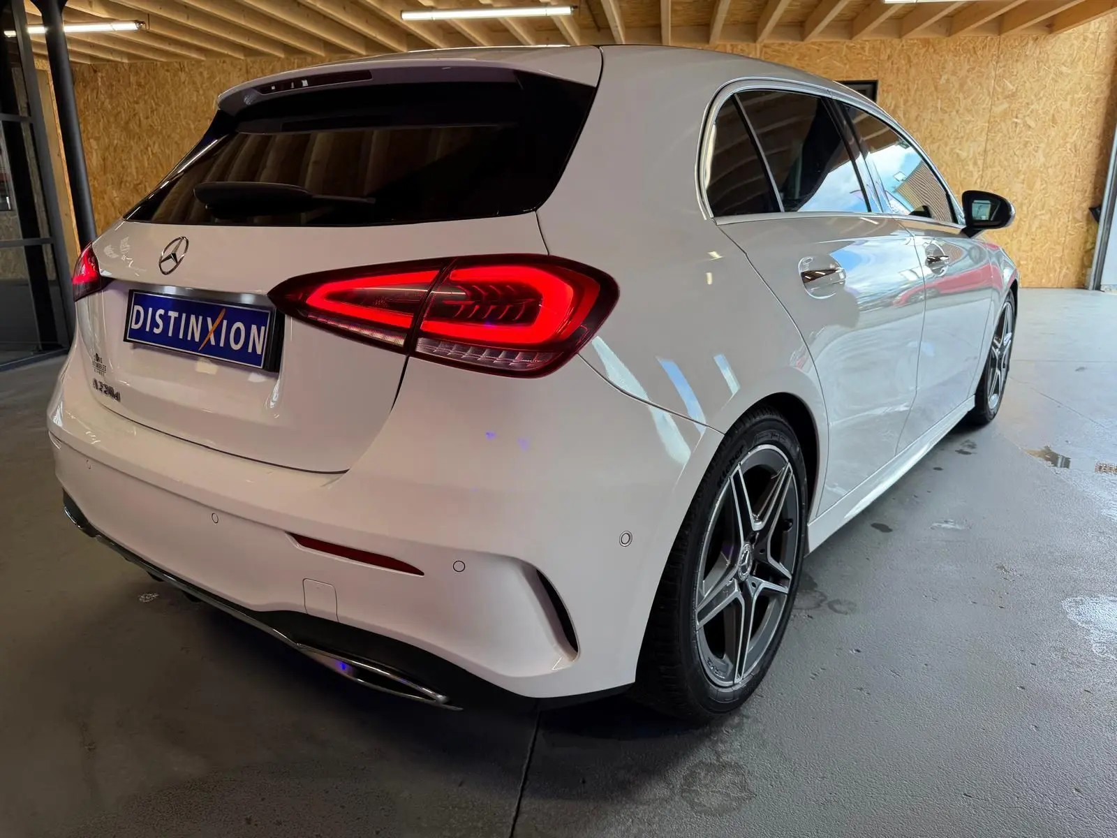 Mercedes Classe A 220D AMG Line blanc vue 3/4 arrière droit, feux arrière allumés et jantes sport visibles.