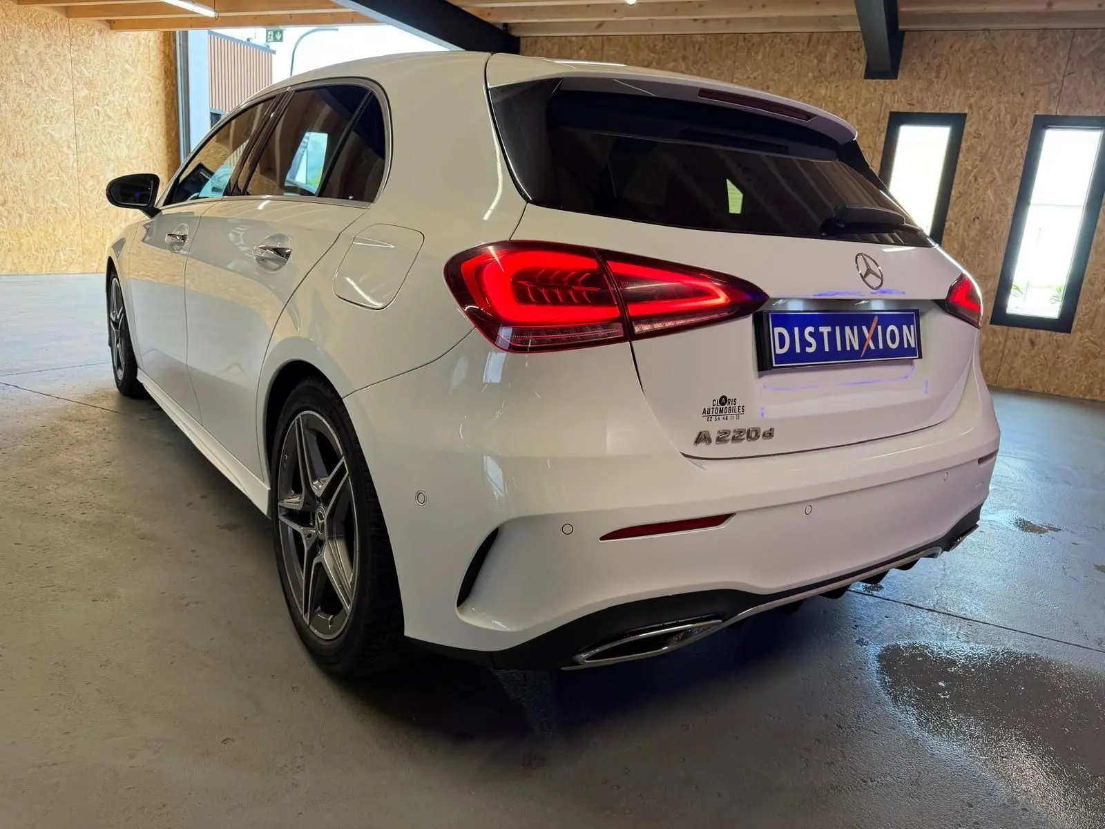 Vue 3/4 arrière droite d'une Mercedes Classe A 220d AMG Line blanche avec feux arrière allumés en intérieur.