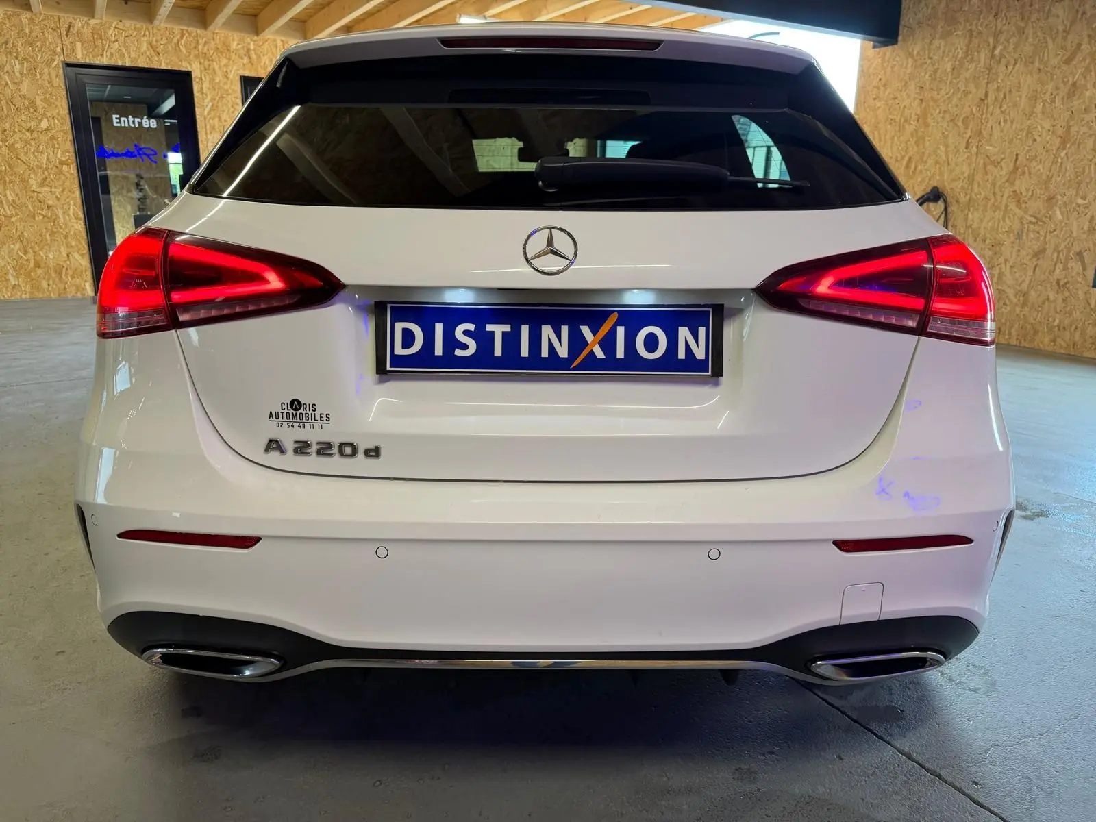 Vue arrière d'une Mercedes Classe A 220d AMG Line blanche avec feux arrière allumés et double sortie d'échappement chromée.