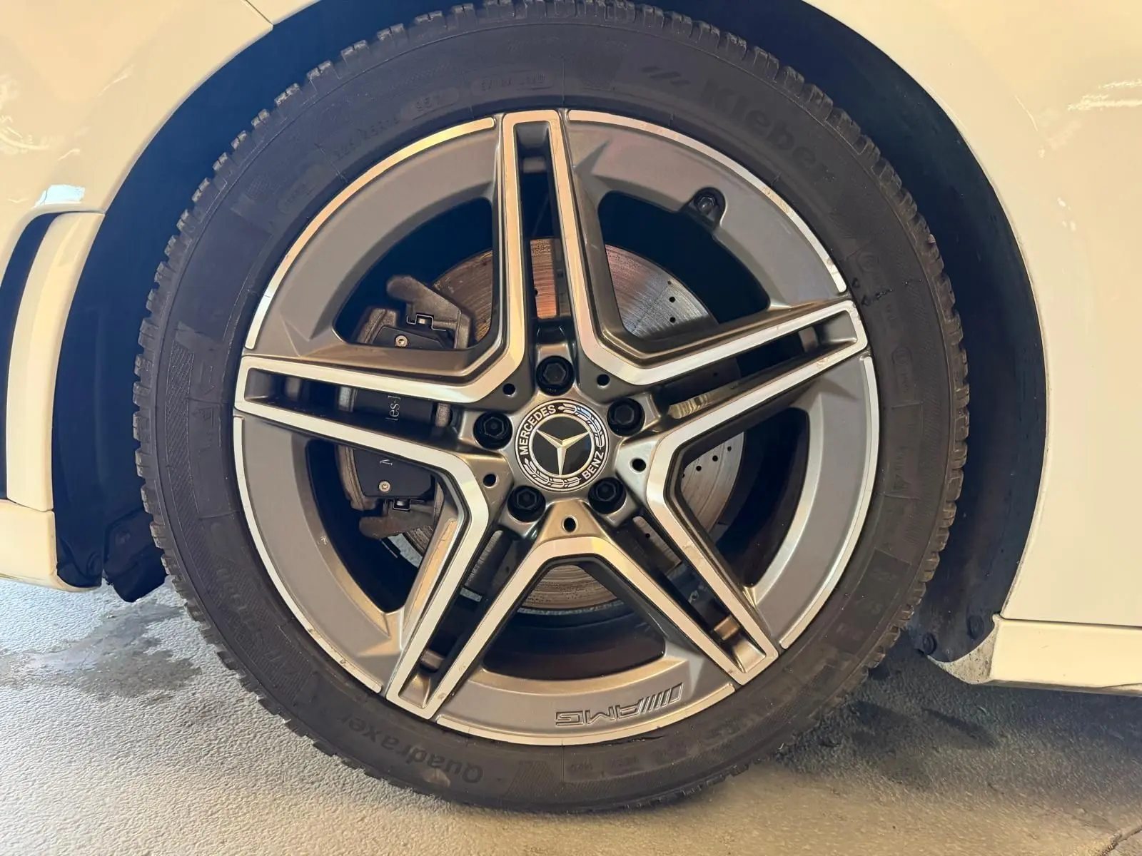 Gros plan sur la jante AMG en alliage gris avec logo Mercedes, montée sur une Mercedes Classe A blanche côté gauche.
