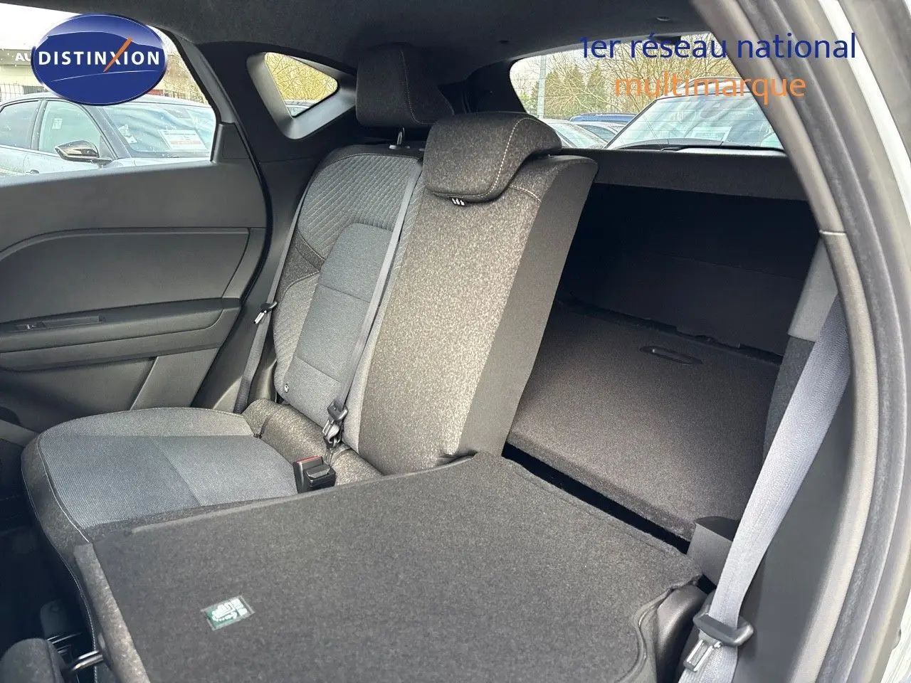 Vue intérieure côté gauche du Renault Captur II hybride 2025, montrant la banquette arrière avec une partie rabattue en tissu gris.