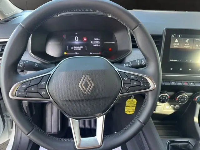 Volant textile noir avec logo Renault au centre, tableau de bord numérique et écran tactile du système multimédia de la Clio V blanche.