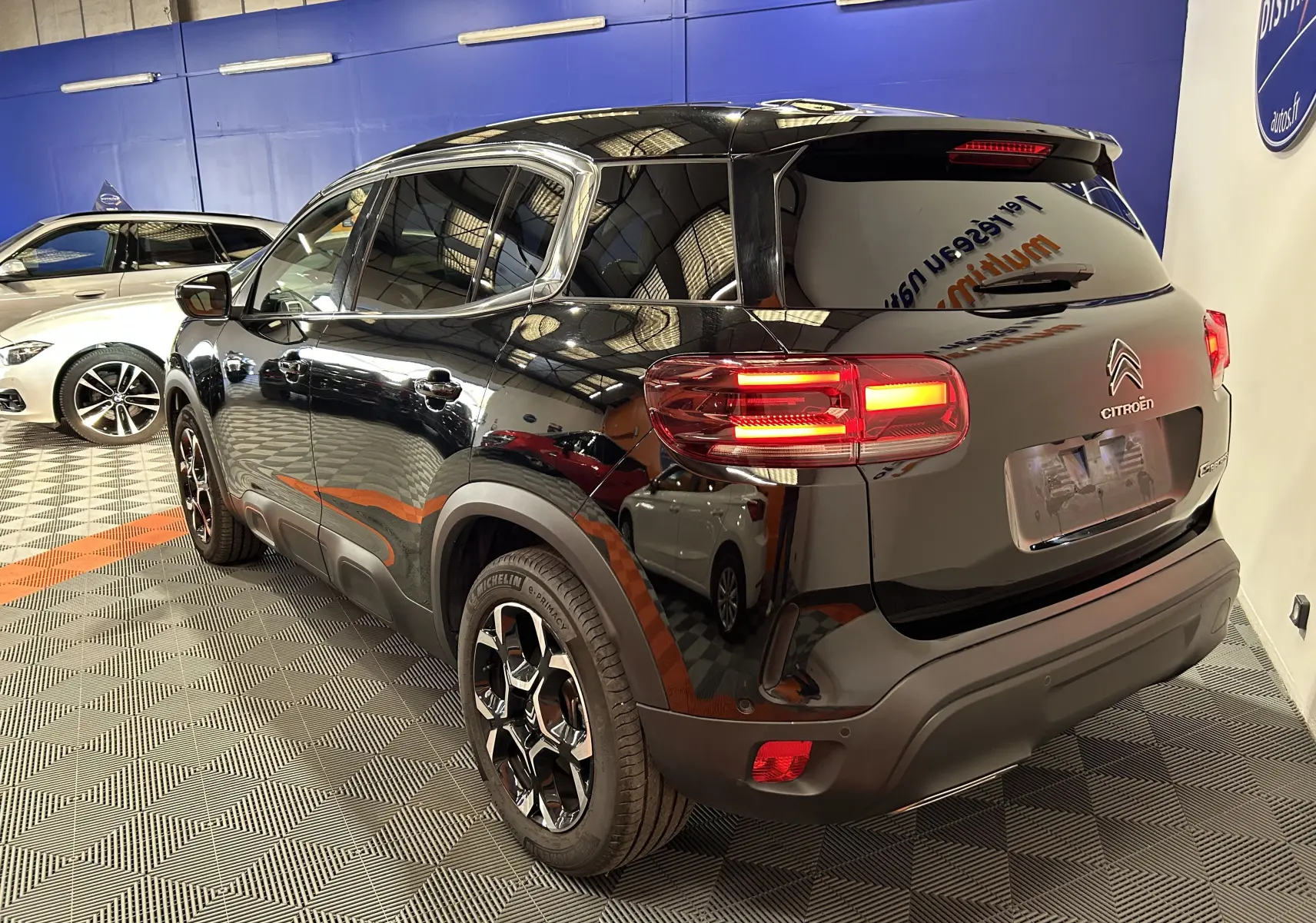 Vue 3/4 arrière droite du Citroën C5 Aircross noir Perla Nera avec feux allumés dans un showroom intérieur.