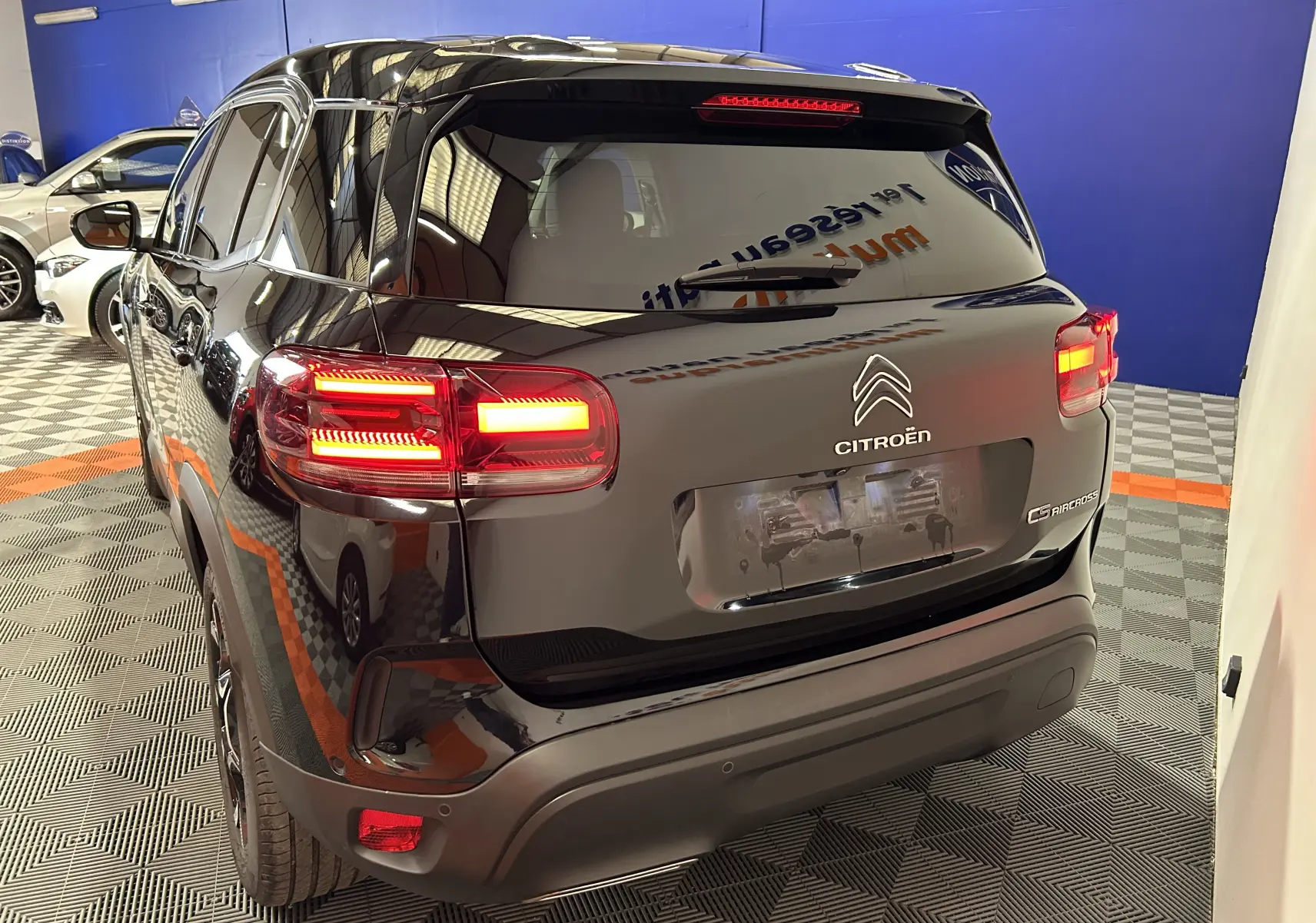 Vue 3/4 arrière d'un Citroën C5 Aircross noir Perla Nera avec feux arrière allumés dans un showroom.