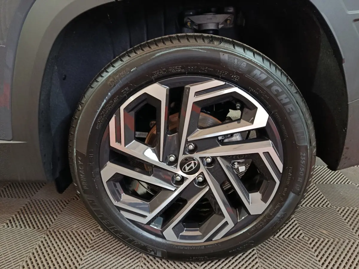 Gros plan sur la roue avant droite du Hyundai Tucson gris foncé, mettant en valeur la jante alliage au design géométrique.