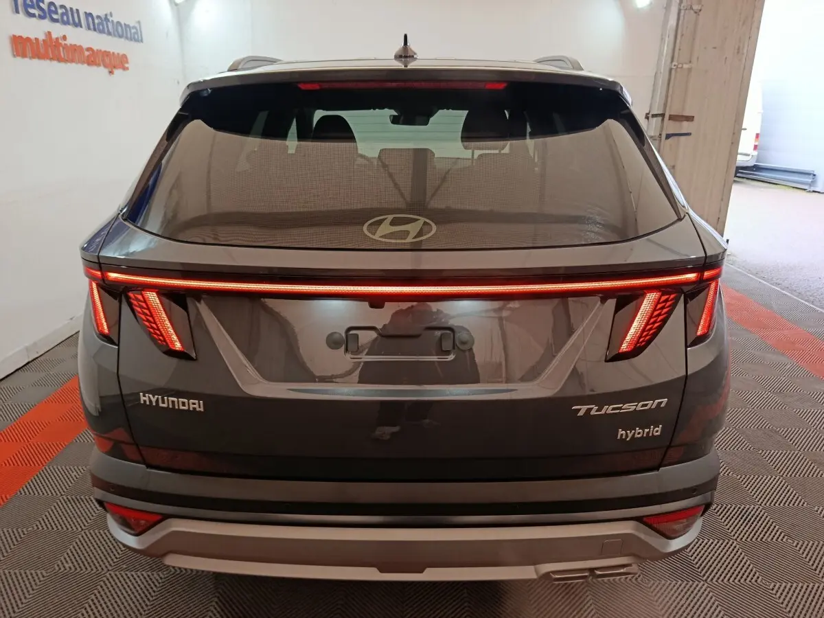 Vue arrière d'un Hyundai Tucson gris foncé 2025 avec feux LED allumés et logo Hyundai visible sur le hayon.