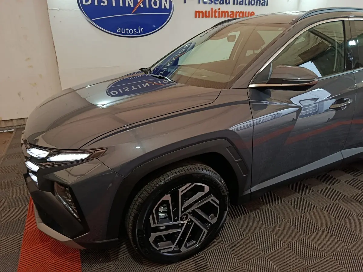 Vue 3/4 avant droit d'un Hyundai Tucson gris foncé avec jantes alliage au design moderne et phares LED allumés.