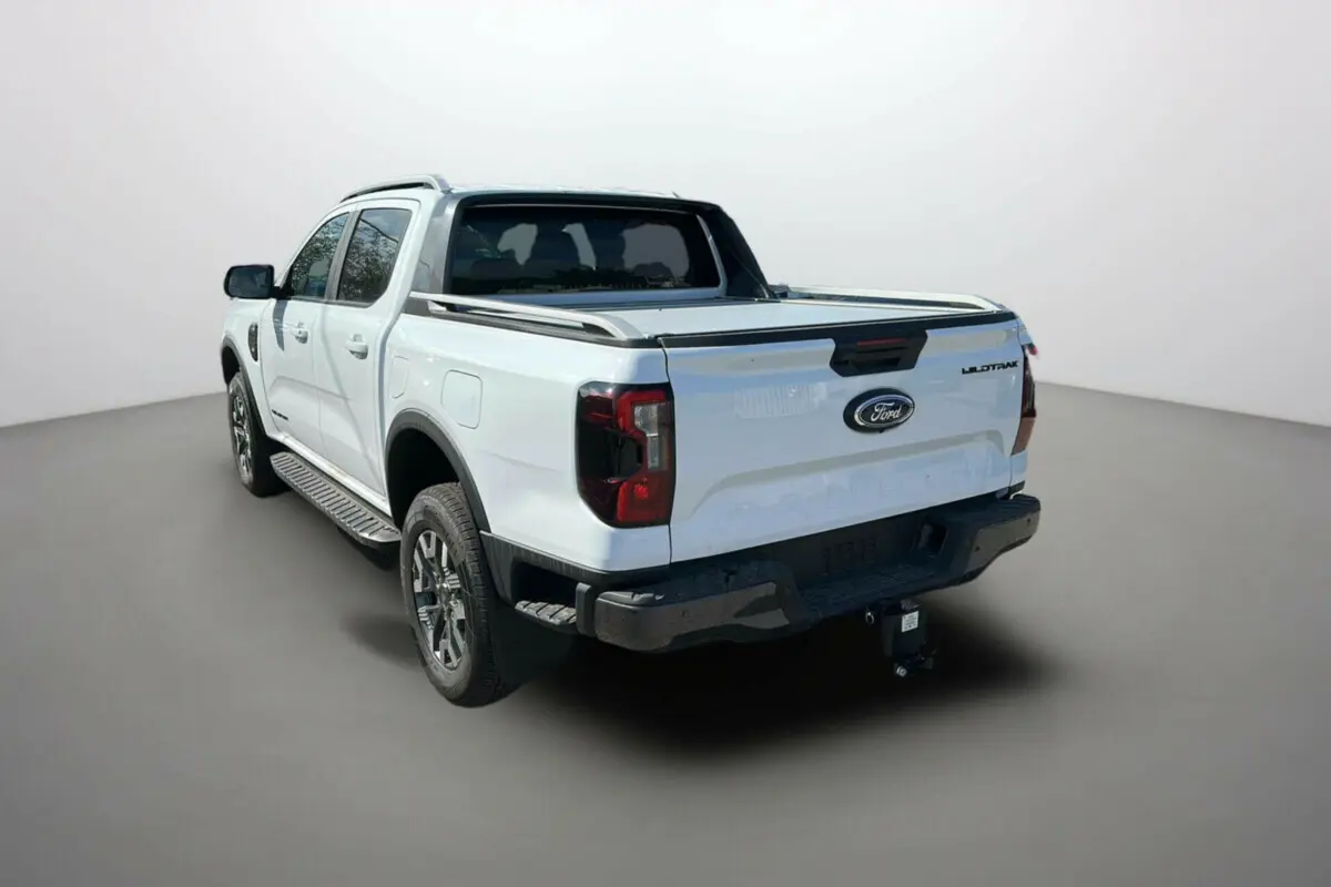 Ford Ranger blanc en 3/4 arrière droit avec benne, attelage et jantes alu 18 pouces visibles.