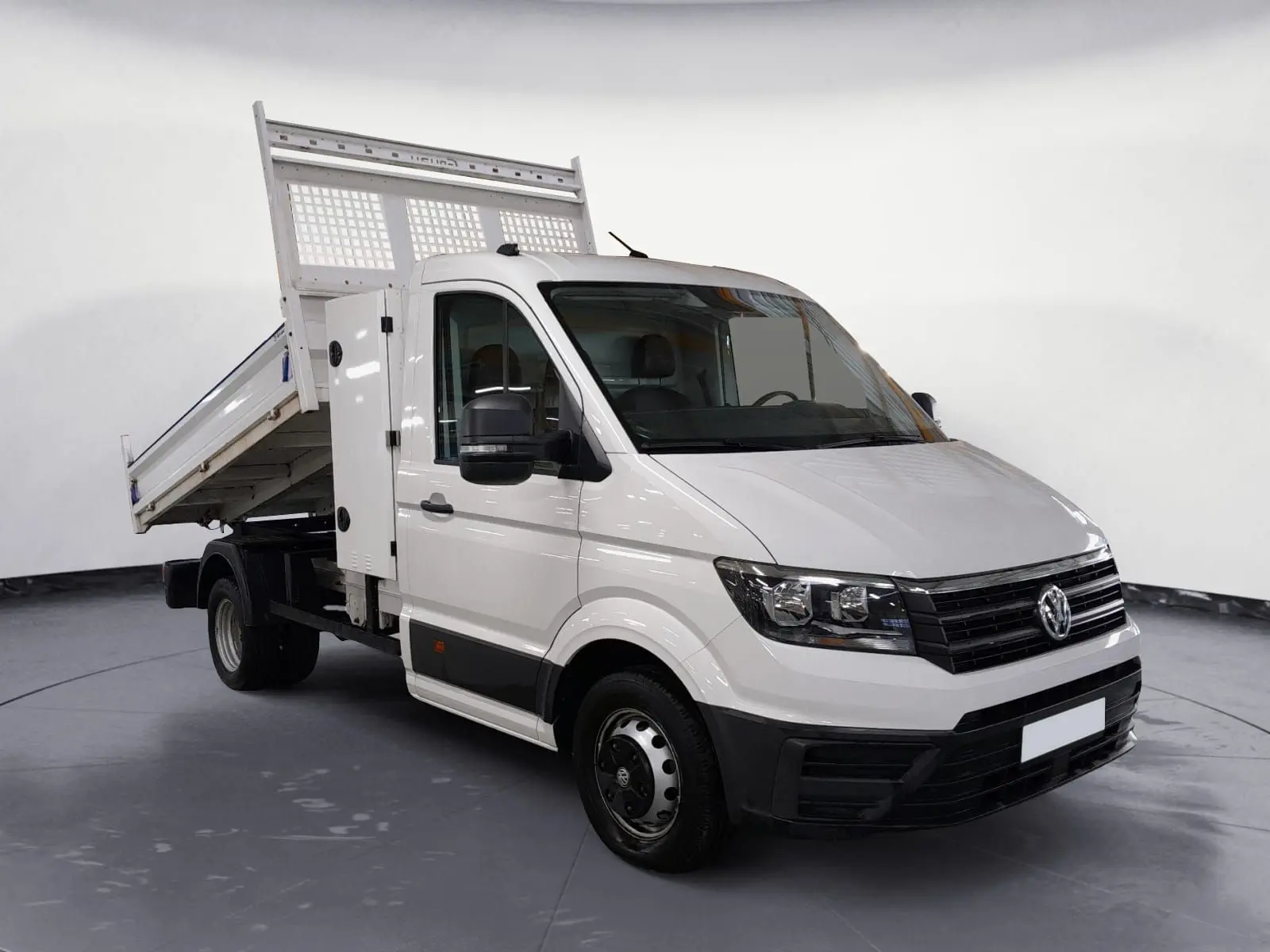 Vue 3/4 avant droite d’un Volkswagen Crafter blanc avec benne relevée, coffre latéral et roues jumelées arrière.