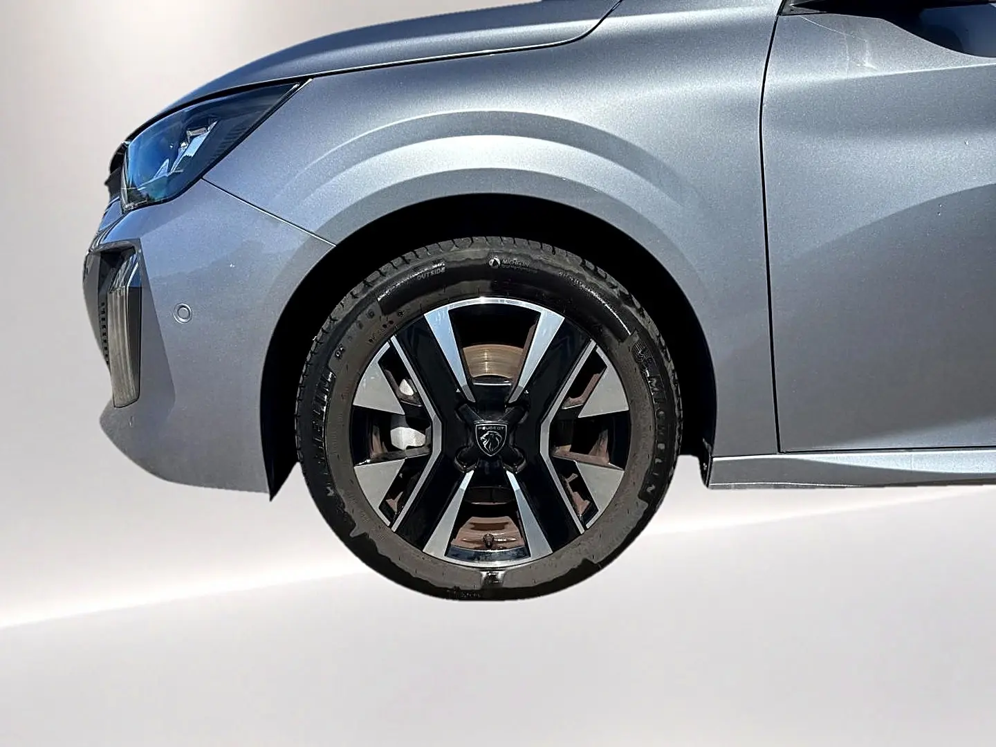 Gros plan sur la roue avant gauche et l'aile avant gris artense d'une Peugeot 208 1.2 100 allure 2025.