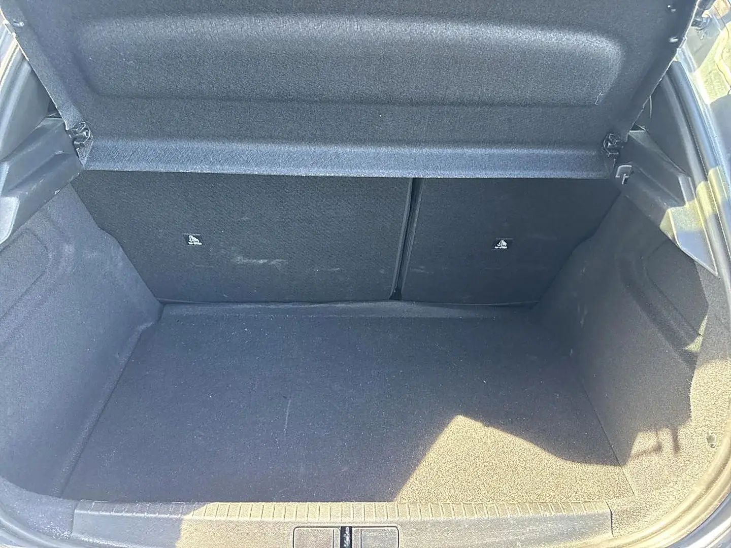 Coffre ouvert de la Peugeot 208 gris artense, vue plongeante montrant l’espace de chargement vide et les dossiers arrière rabattables.