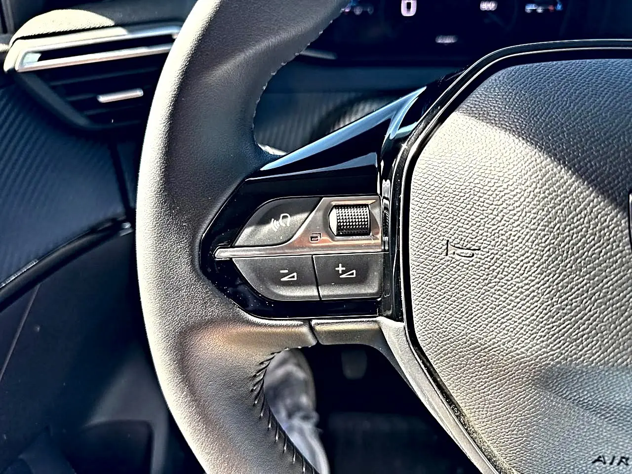 Gros plan sur le volant noir de la Peugeot 208 1.2 100 Allure, montrant les commandes audio au volant côté gauche.