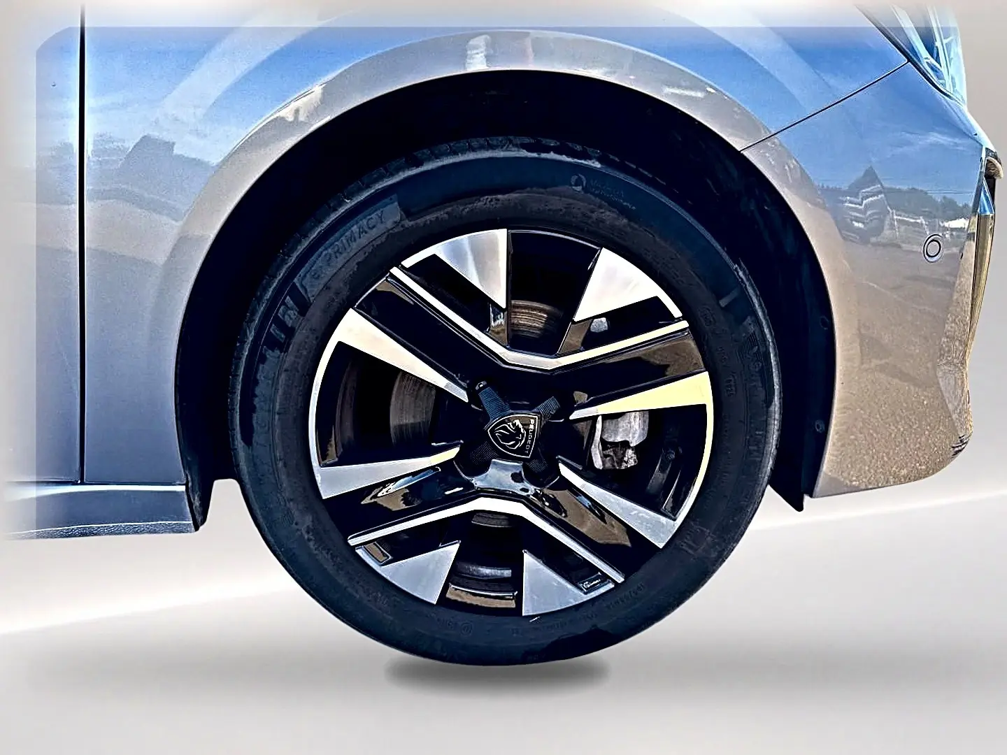 Gros plan sur la roue avant droite avec jante alu bicolore d'une Peugeot 208 gris artense, partie de la carrosserie visible.