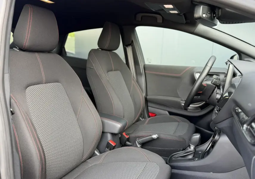 Vue intérieure côté gauche du Ford Puma 2024 Ecoboost ST Line, sièges tissu gris avec surpiqûres rouges et console centrale.