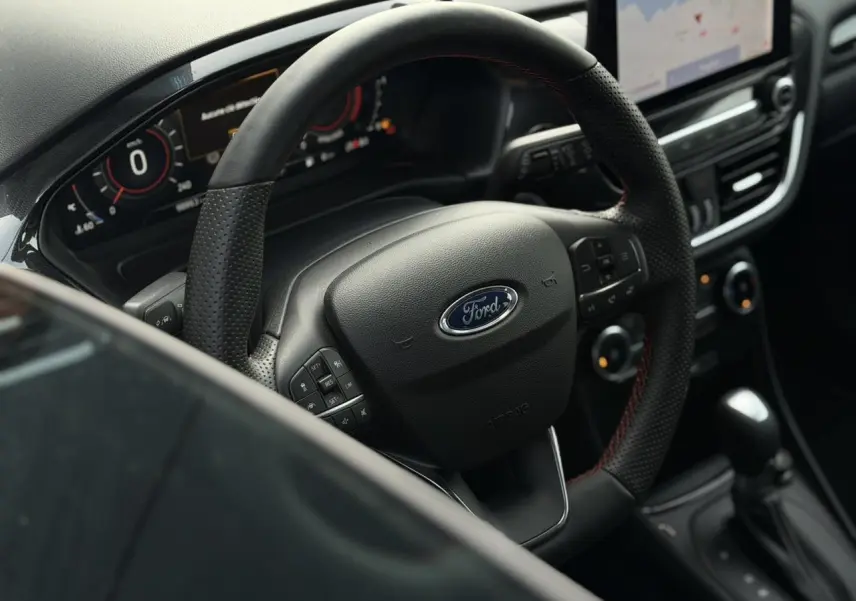 Vue intérieure centrée sur le volant ST-Line perforé du Ford Puma 2024 avec tableau de bord numérique et écran tactile.