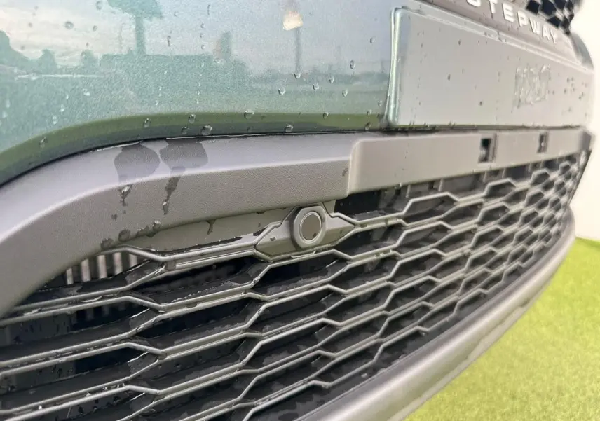 Gros plan sur la calandre noire et la face avant vert cèdre de la Dacia Sandero III Stepway avec logo Stepway visible.
