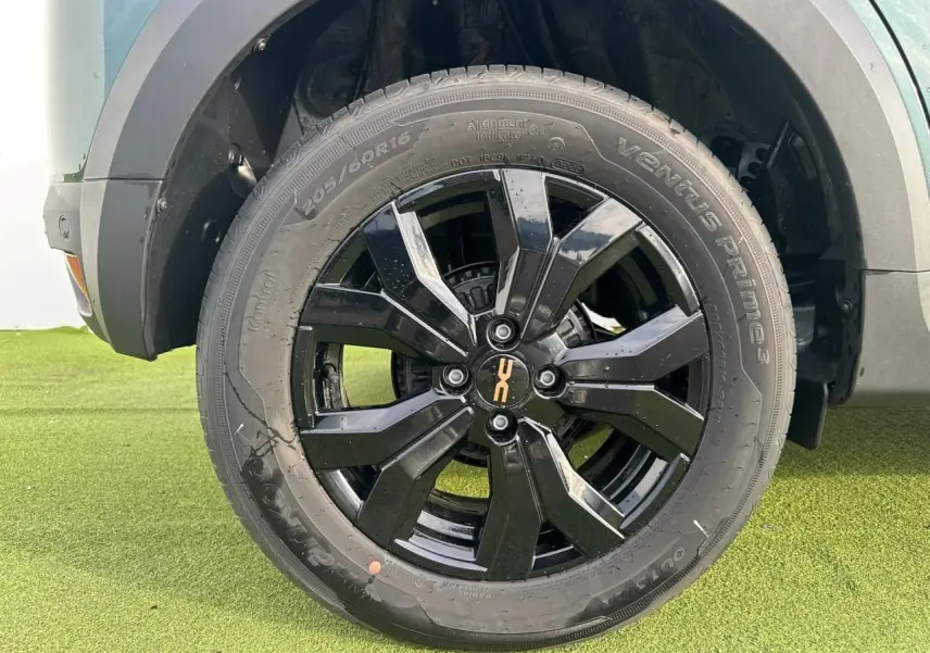 Gros plan sur la roue avant droite de la Dacia Sandero III Stepway en Vert Cèdre avec jante aluminium noire brillante.