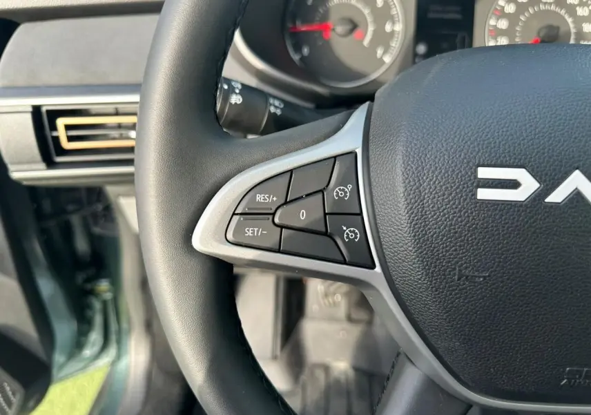 Gros plan sur le volant noir de la Dacia Sandero III Stepway avec commandes de régulateur de vitesse, intérieur gris.