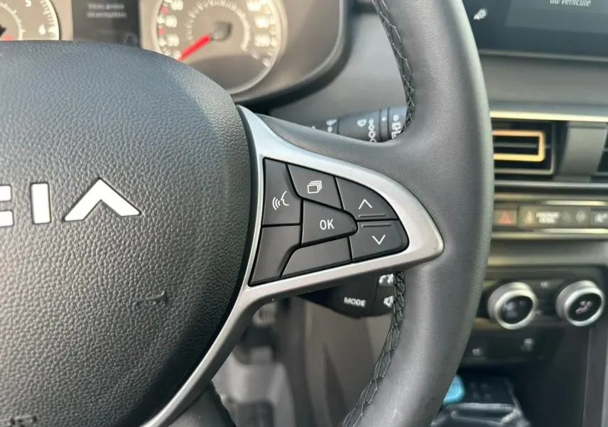 Gros plan sur le volant noir de la Dacia Sandero III Stepway avec commandes multifonctions et tableau de bord partiel.