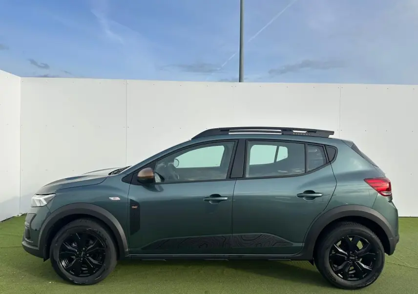 Profil latéral gauche de la Dacia Sandero Stepway 2025 en vert cèdre avec jantes noires et barres de toit brun cuivré.