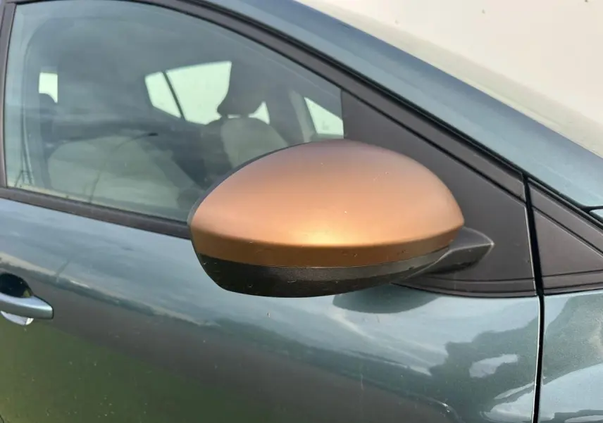 Gros plan sur le rétroviseur brun cuivré côté conducteur d'une Dacia Sandero III Stepway Vert Cèdre.