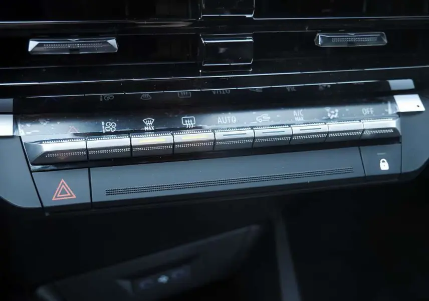 Gros plan sur la console centrale de la Renault Clio VI bleu iron, mettant en valeur les commandes de climatisation automatique et les boutons multifonctions.