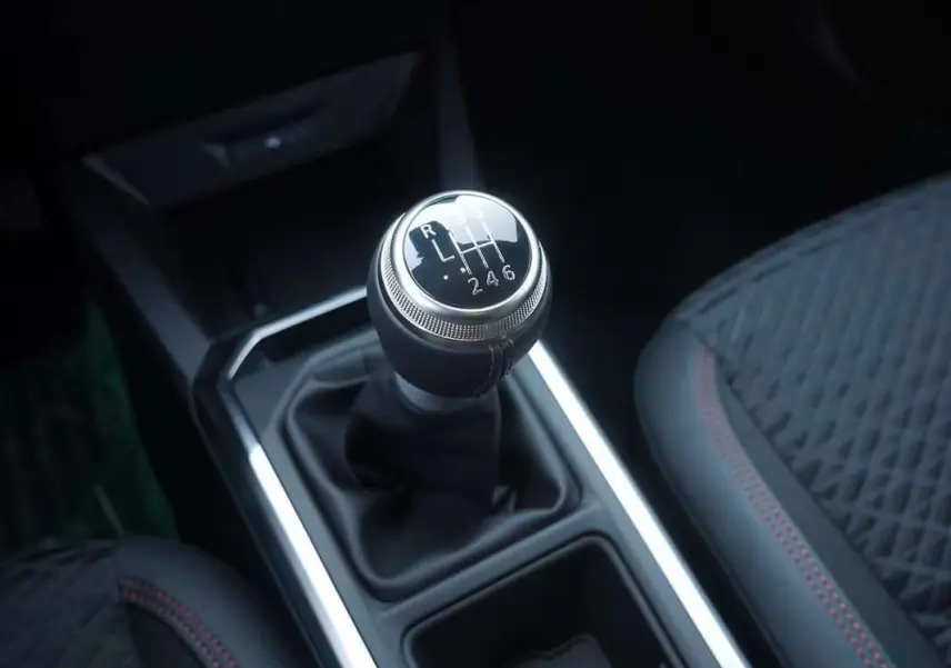 Gros plan sur le levier de vitesses manuel de la Renault Clio VI bleu iron, avec sellerie noire et surpiqûres rouges.