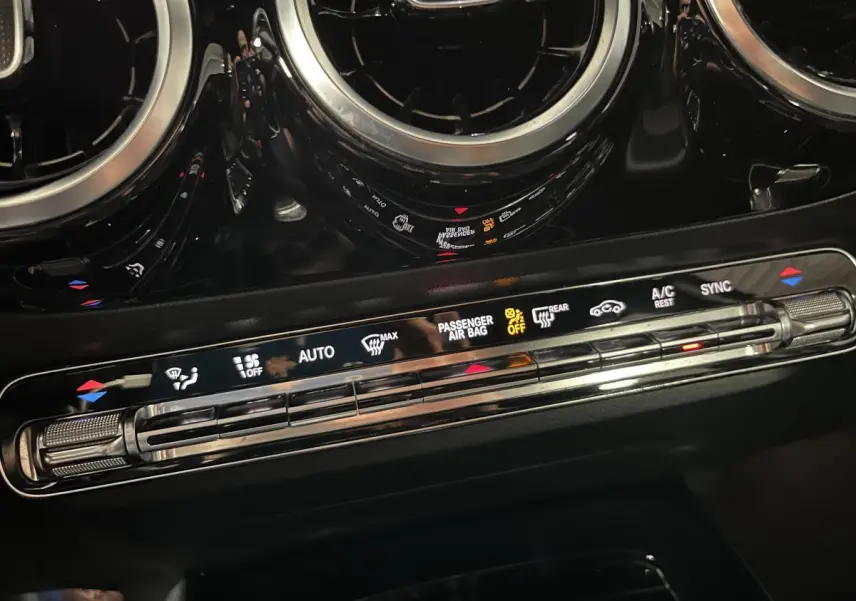 Détail de la console centrale noire du Mercedes Classe B 180 d 2019 avec commandes climatisation et aérateurs ronds chromés.