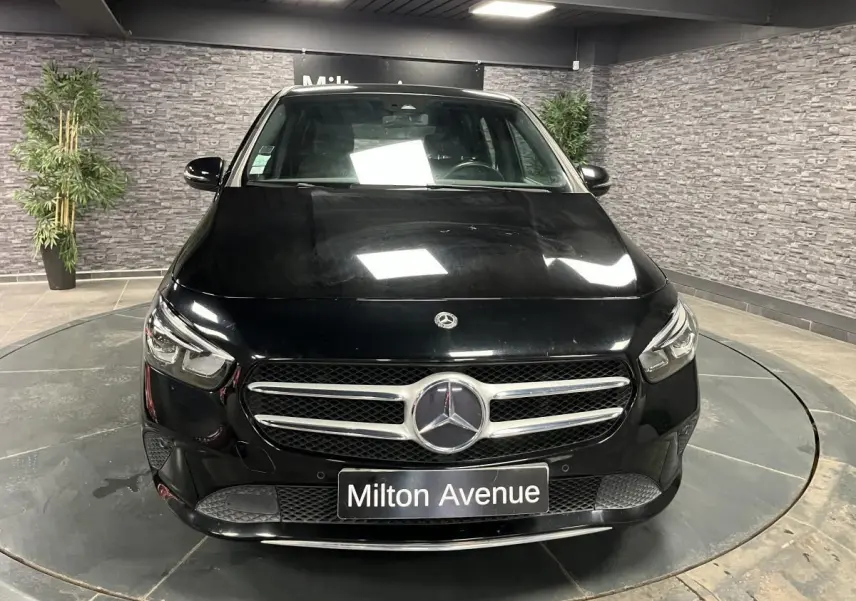 Vue avant d'une Mercedes Classe B noire avec calandre chromée et logo central, sur plateau tournant intérieur.